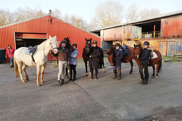 5 unge mennesker poserer foran rideskole med hver sin hest