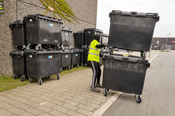 Servicemedarbejder som håndterer store affaldscontainere